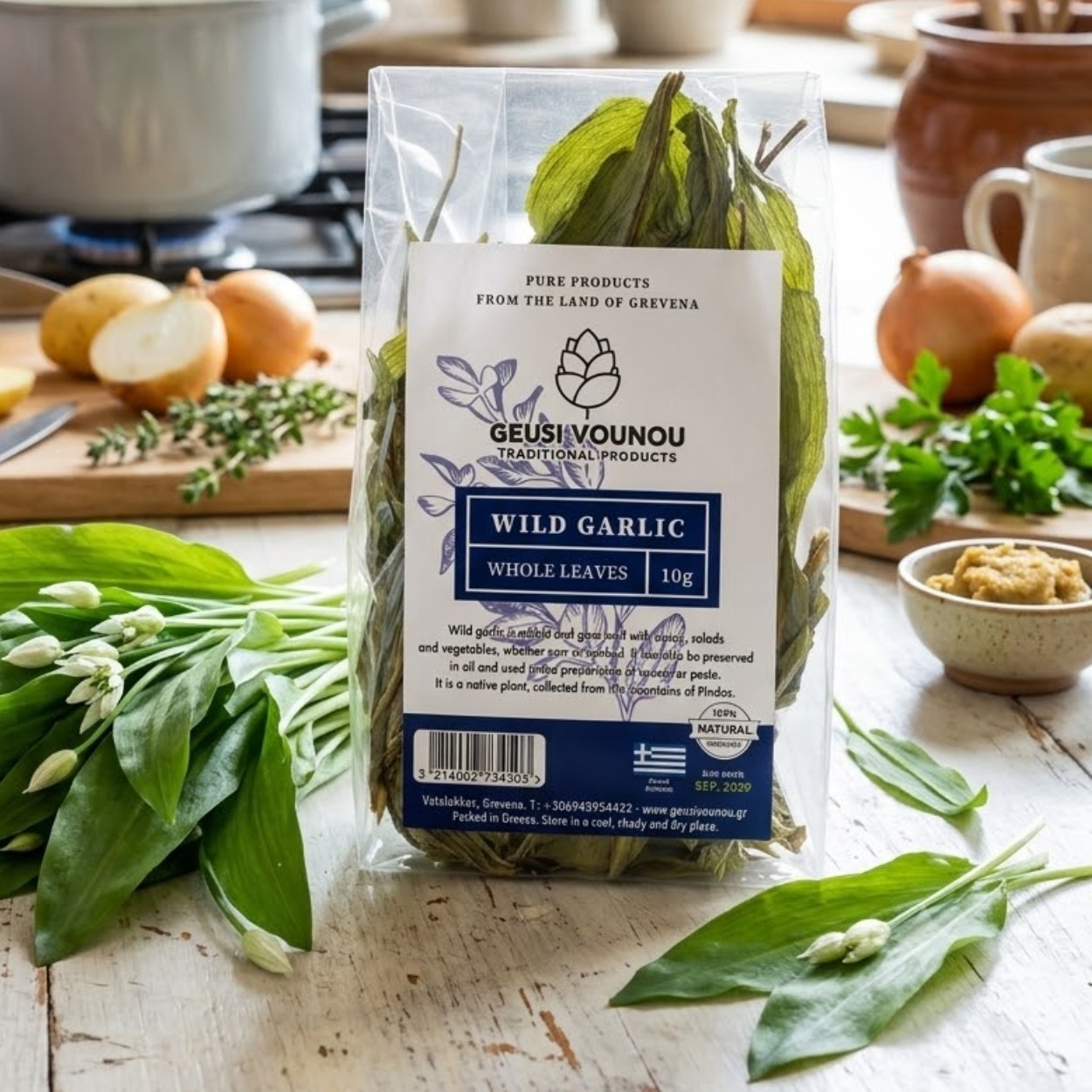 Balení sušeného medvědího česneku Geusi Vounou Wild Garlic na rustikálním kuchyňském stole v prosvětlené kuchyni, v popředí čerstvé listy a poupata medvědího česneku, v pozadí příprava polévky na sporáku.